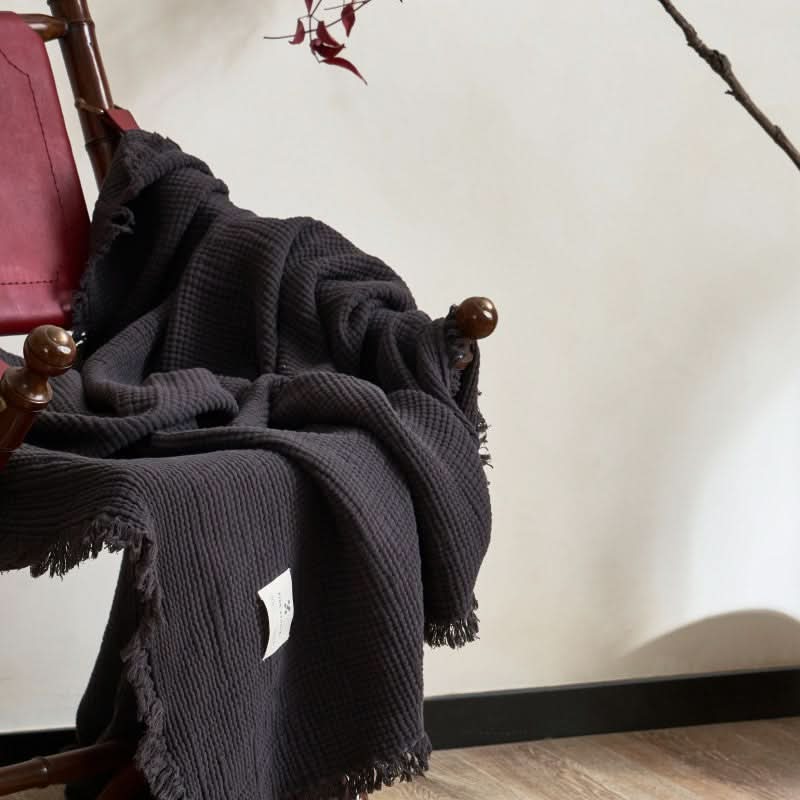 Cozy Textured Cotton Throw Blanket in dark gray, draped on a chair with fringed edges.